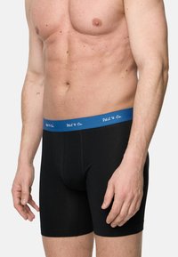 Svarta boxerkalsonger i bomull med ett blått midjeband som har vit text. Designen är figurnära, med en slät yta och sömmar.