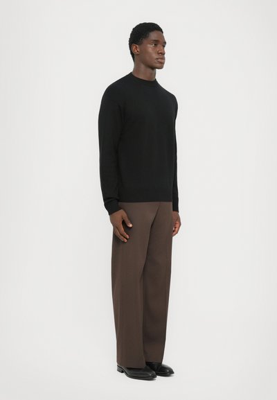 Pulover negru tricotat cu guler rotund, asortat cu pantaloni largi maro și pantofi din piele negri. Design simplu, ajustat, cu manșete ribate.