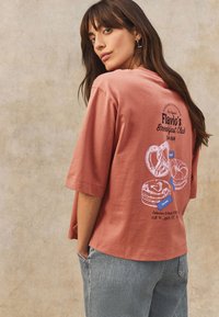 Camiseta extragrande de color rosa, hecha de algodón, con estampado gráfico blanco de pasteles y texto en la parte trasera, mangas cortas y corte holgado.