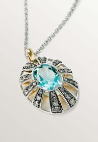 Collar de plata con una gran gema ovalada de color azul claro rodeada de pequeñas piedras negras, con un acento dorado en el gancho del colgante.