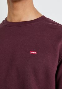 Bordeauxfärgad bomullshuvtröja med rundad halsringning, med ett litet rött Levi's-logotypmärke placerat på vänster bröst.