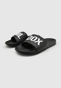 Zwarte slippers met een brede band met contrasterende witte letters. Texturen: glad bovenmateriaal, vlakke rubberen zool. Eenvoudig ontwerp, casual pasvorm.