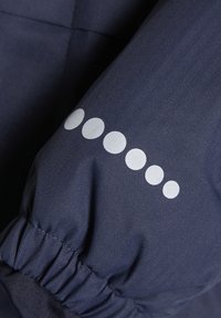 Mørkeblå jakke med ærme i hønsenetex og elastisk mansjett, dekorert med fem hvite sirkulære prikker i diagonalt mønster.