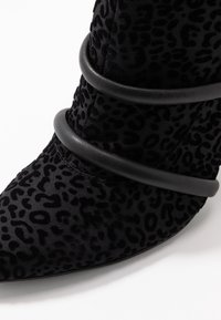 Bottines à talons hauts en imprimé léopard noir avec un bout pointu. Présente des bandes noires élégantes autour de la cheville, mettant en valeur sa surface texturée.