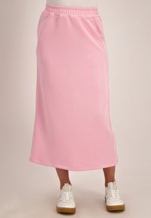 Lichtroze midi-rok met elastische tailleband en zijzakken, gedragen met witte sneakers en lichtbruine zolen.