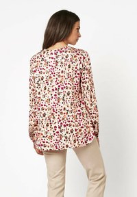 Langärmlige Bluse mit einem hellrosa Hintergrund und einem Blumenmuster in Schattierungen von Rot, Braun und Schwarz; glattes Material, abgerundeter Saum.