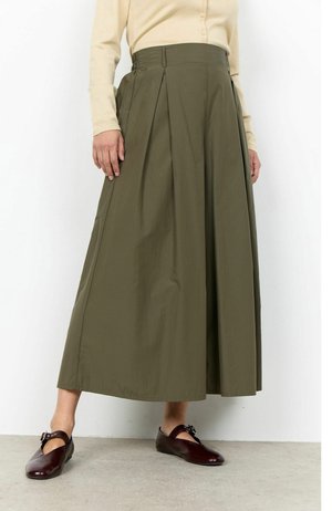 High-Waist olivgrüner A-Linien-Rock mit vorderen Falten, kombiniert mit beigefarbenem Langarmtop und dunkelbraunen Mary Jane Schuhen auf Betonboden.
