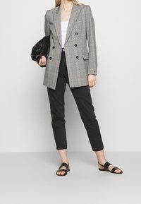 Blazer de cuadros gris con doble botonadura y botones negros, combinado con jeans negros y sandalias negras. Incluye una blusa blanca y un bolso negro texturizado.