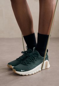 Grønne atletiske sko med en tekstureret overdel, hvid sål og beige detaljer, parret med sorte sokker, på en neutral baggrund.