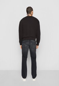 Sweat-shirt noir à col rond, avec des poignets côtelés, associé à un jean bleu foncé avec poches arrière. Design simple, coupe décontractée. Chaussures blanches.