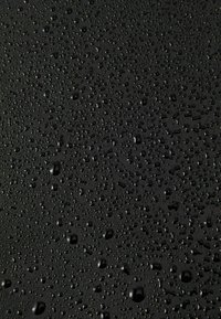 Schwarze Oberfläche mit zahlreichen Wassertropfen unterschiedlicher Größe, die eine glänzende Textur erzeugen und das Licht leicht reflektieren.