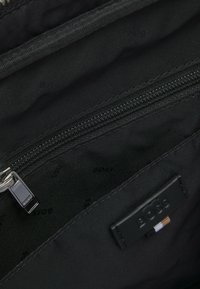 Sort stofpose indvendigt med lynlåslomme, logoetiket og glat tekstur. Synlige syninger og detaljer på lynlåshardware.