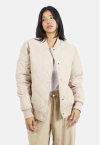 Veste bomber matelassée beige avec un col côtelé, fermeture à boutons-pression et poches latérales. Texture douce avec un motif en losanges.