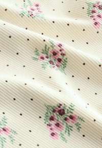 Tela cremosa acanalada con pequeños lunares negros y racimos de flores rosas con hojas verdes esparcidas por la superficie.