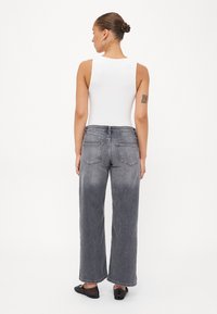 Grå vida jeans med en blekt tvätt, med bakfickor och hög midja, kombinerat med en ärmlös vit topp och svarta ballerina.