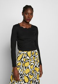 Top nero a maniche lunghe con scollatura ornata in pizzo, abbinato a una gonna bianca con un motivo astratto giallo e nero.