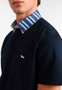 Granatowa koszulka polo z wzorzystym niebiesko-różowym kołnierzykiem, z małym białym wyszywanym logo na piersi.