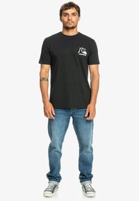Black cotton t-shirt with a round neckline and short sleeves, featuring a white logo on the left chest, paired with blue denim jeans.