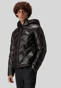 Musta untuvatakki, jossa on huppu, timanttikuvioinen tikkaus ja kiiltävä viimeistely. Vetoketjusuljenta ja hillityt merkkikoristeet olkapäällä.