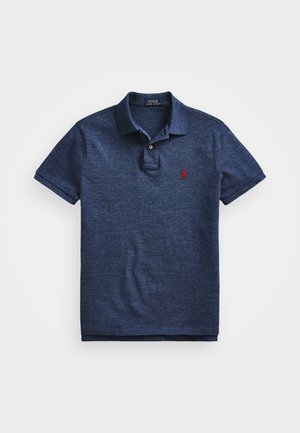Baju polo biru navy terbuat dari kain dengan tekstur. Memiliki kerah klasik, placket dua butang, dan logo merah kecil di dada kiri.