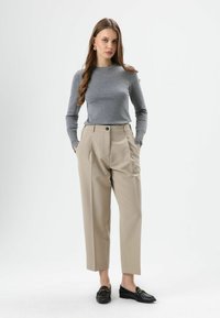 Gray long-sleeve shirt, beige pleated trousers with side pockets, and black loafers with gold hardware. Smooth fabric, tailored fit.