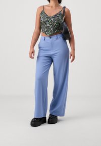 Černý květinový crop top s tenkými ramínky, v kombinaci s širokými světlomodrými kalhotami a černými botami na robustní podrážce. Jednoduchá kabelka přehozená přes rameno.