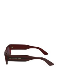 Occhiali da sole in plastica rossa con montatura rettangolare e stecche eleganti, con logo Calvin Klein e dettagli metallici sulle aste.