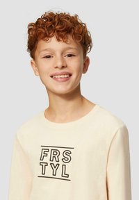 Hellbeige Langarm-T-Shirt mit einem schwarzen geometrischen Druck "FRSTYL" in der Mitte. Weicher Stoff mit einem entspannten Halsausschnitt.