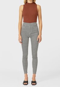 Bruine mouwloze top, hoog op de taille zwarte en witte houndstooth skinny broek, gladde textuur en open teen zwarte hoge hakken sandalen.