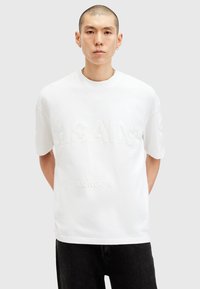 White cotton t-shirt featuring embossed "SAINT LAURENT" and "LONDON" text. Short sleeves, crew neck, relaxed fit, minimalistic design.