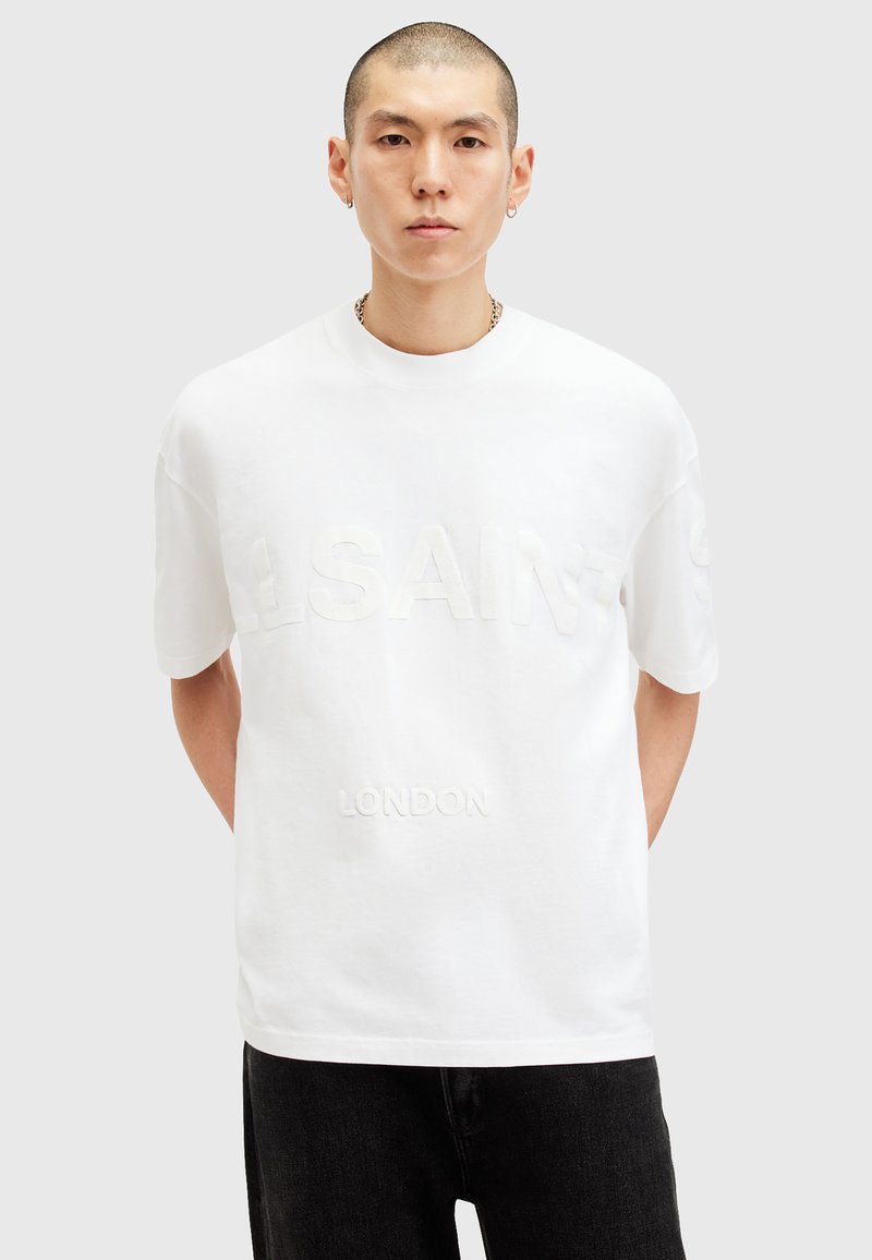 White cotton t-shirt featuring embossed "SAINT LAURENT" and "LONDON" text. Short sleeves, crew neck, relaxed fit, minimalistic design.