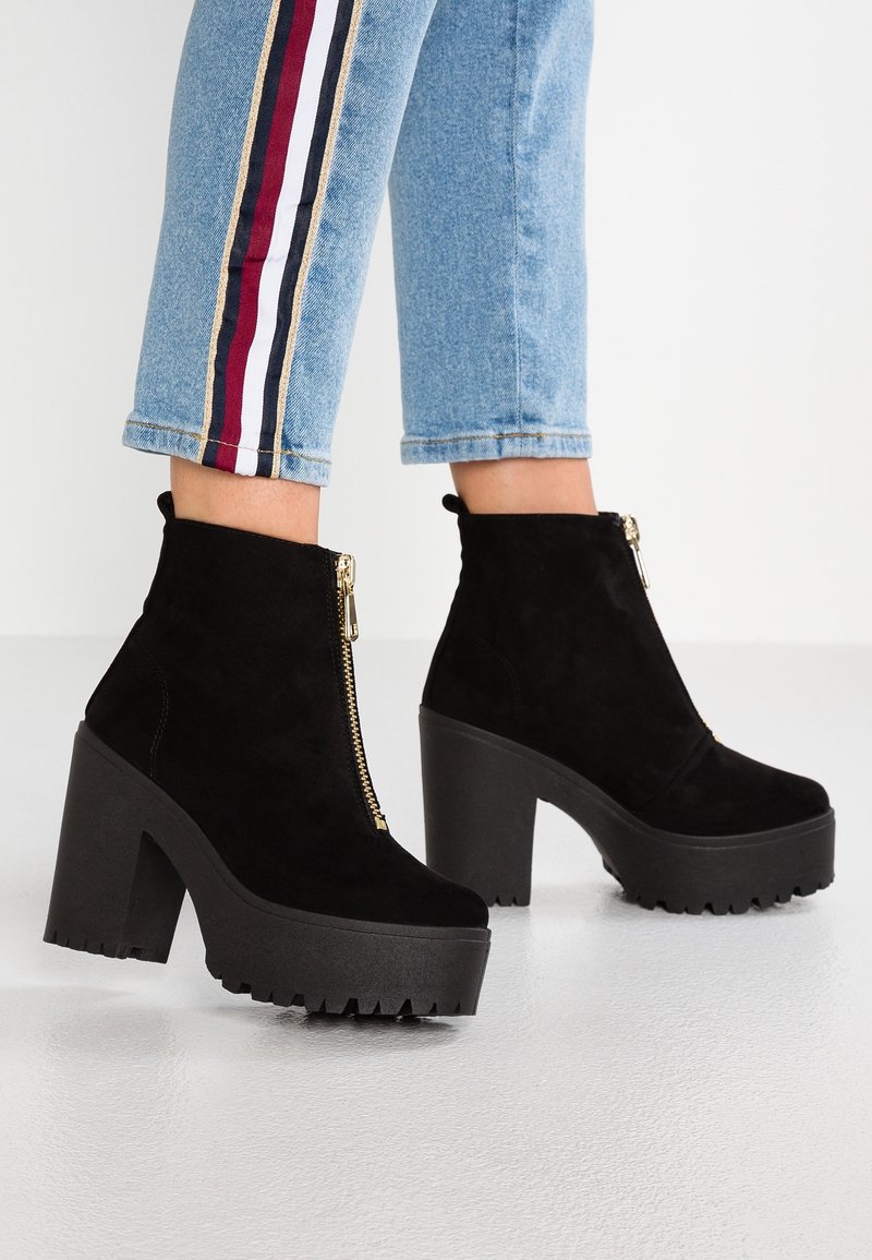 Mustat mokkanahkaiset nilkkurit, joissa on paksu, teksturoitu pohja ja korkea palikkakorko. Varusteena edessä vetoketju ja terävä siluetti.