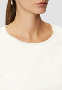 Weißes Shirt mit kurzen Ärmeln und Rundhalsausschnitt, aus weichem Baumwollstoff, glatte Textur und dezente Nähdetails.