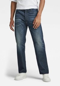 Denim jeans in dark blue wash with a straight leg design, five-pocket styling, and subtle fading; paired with white sneakers.