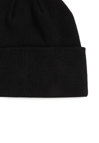 Černá pletená čepice s vroubkovaným vzorem a ohrnutým lemem, detailní záběr na texturu látky a švy.