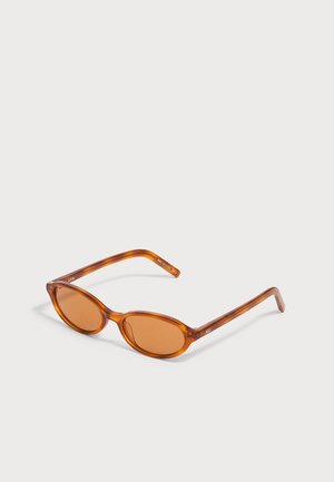 Gafas de sol de forma ovalada con lentes tintadas en ámbar y monturas marrones con efecto carey, apoyadas sobre una superficie gris claro.