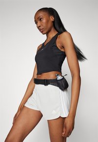 Schwarzes Sporttanktop mit Racerback-Design, kombiniert mit hellgrauen Shorts, die weiße Streifen und ein Adidas-Logo aufweisen. Schwarzer Trinkflaschen-Gürtel.
