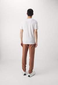 Weißes kurzärmliges Hemd aus leichtem Material, kombiniert mit braunen geraden Hosen. Die Schuhe sind schwarz-weiß mit einem runden Design.
