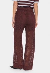 Pantaloni in pizzo borgogna con un motivo a maglia aperta, vita alta e taglio ampio. Presentano una finitura testurizzata e un design minimalista.