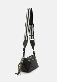 Schwarze Lederhandtasche mit einem Reißverschlussfach, ausgestattet mit einem dekorativen Quasten. Begleitet von einem geflochtenen Tragegurt mit schwarz-weißen Streifen.