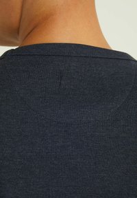 Häivän henkilön niska ja yläselkä, jossa on tumma harmaa kangaspaita, jossa näkyvät saumat ja hienovarainen rakenne.