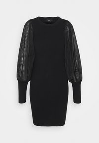 Robe noire longueur genoux avec corps en maille côtelée et manches longues bouffantes transparentes finissant par des poignets ajustés.