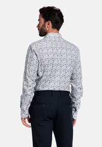Lange mouwen overhemd met een witte achtergrond, met een geweven bloemenpatroon in blauw en bruin. Gecombineerd met donkere broek.