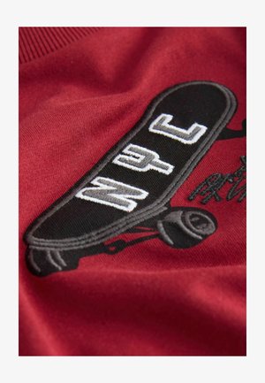 Punane kangas musta rulalaudade mustriga ning tekstiga "NYC." Rulalaudal on valged ja hallid detailid ning nähtav on kerge tekstuur.