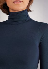 Tmavě modrý rolák vyrobený z hladké, pružné látky. Má vysoký límec se zdobením z nařaseného materiálu, přiléhavý střih a dlouhé rukávy.