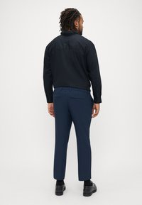 Marineblaue Hosen mit tailliertem Schnitt, ausgestattet mit zwei Gesäßtaschen und einem leichten, glatten Stoff; kombiniert mit einem schwarzen Langarmhemd.