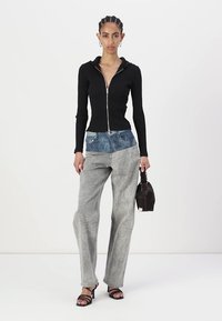 Svart zip-up hettegenser med lange ermer, kombinert med lysegrå mønstrede jeans med blå denim liv. Modell som holder en liten veske.