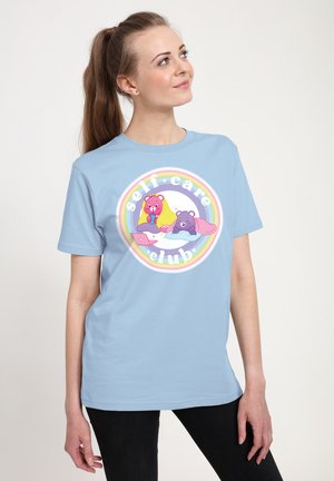 Lyseblå T-shirt lavet af bomuld med et rundt grafik, der viser farverige tegneserie-bjørne og teksten "self-care club" inden i en regnbuecirkel.