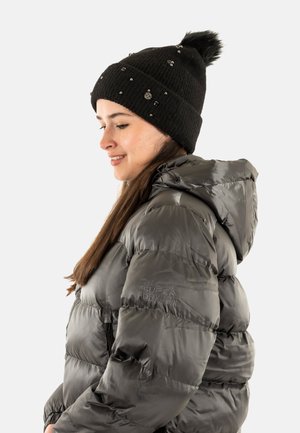 Cappello a maglia nera con pompon e decorazioni; giacca puffer grigia con chiusura a zip e cappuccio; logo del brand visibile sulla manica.
