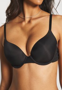 Soutien-gorge noir rembourré avec armatures, en tissu lisse, avec des bretelles réglables et un décolleté plongeant, présentant un look minimaliste sans coutures.